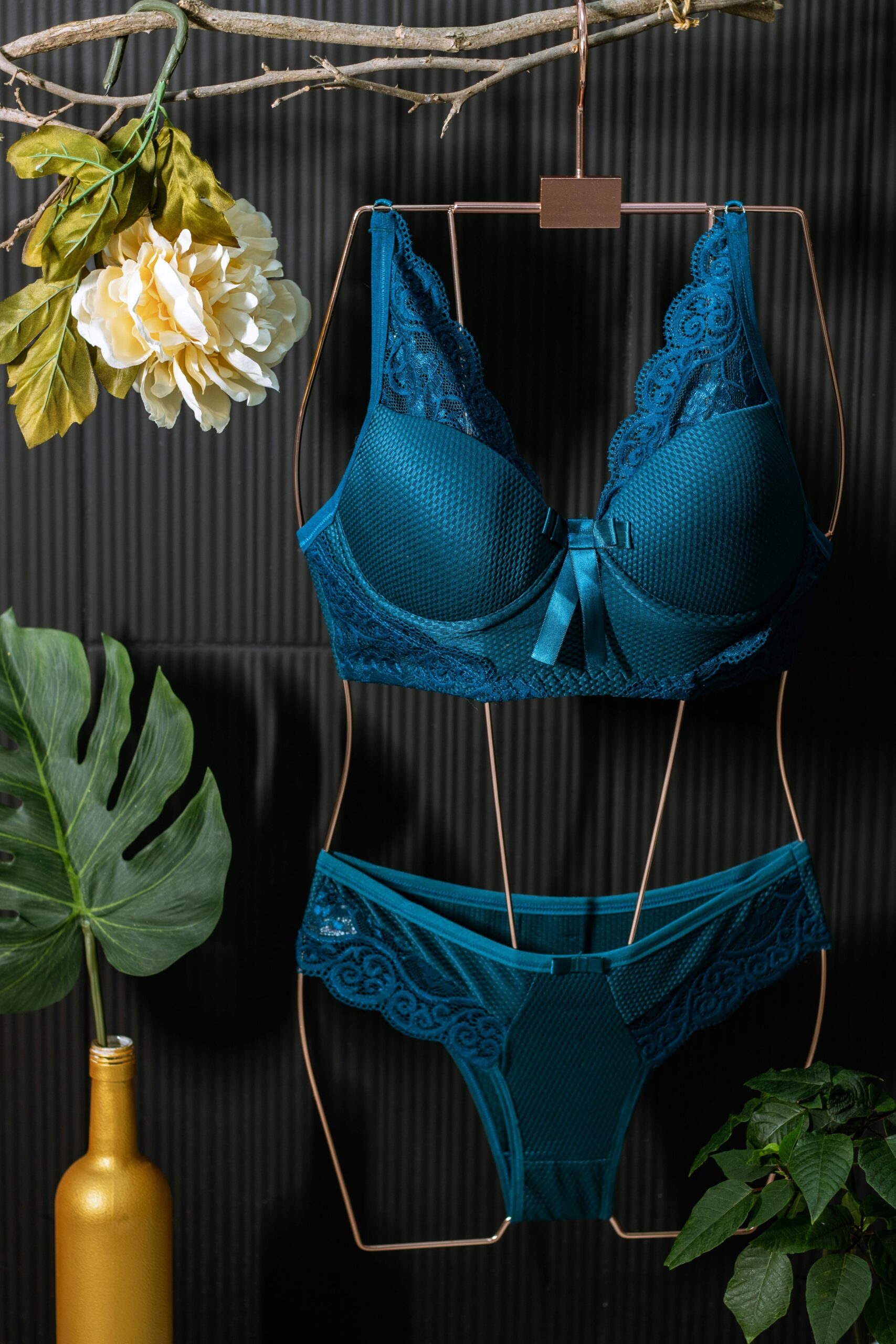 Blue lingerie set on hanger with decorative leaves and flowers against dark background.
